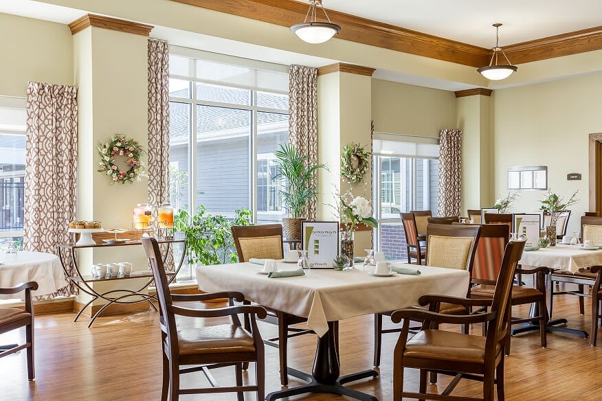 A well-lit dining area with neatly arranged tables and chairs, featuring large windows and tasteful decorations.