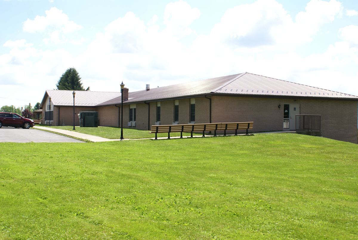 A single-story brick building with a metal roof, surrounded by a well-maintained lawn and benches in the foreground.