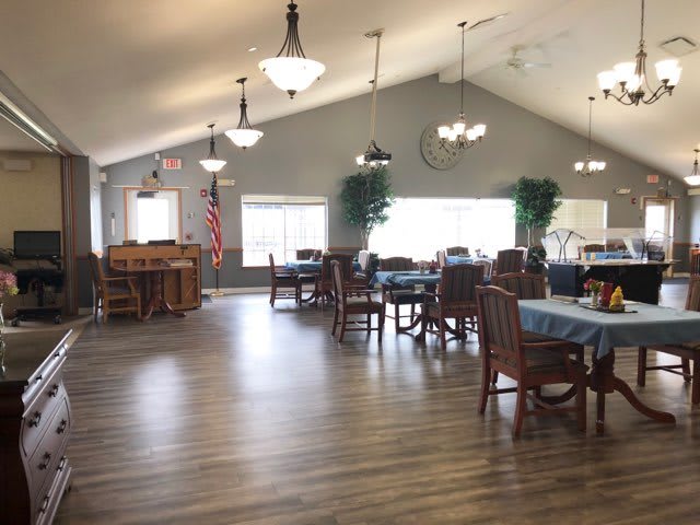 A spacious dining area with tables and chairs, featuring wooden flooring and ceiling lights.