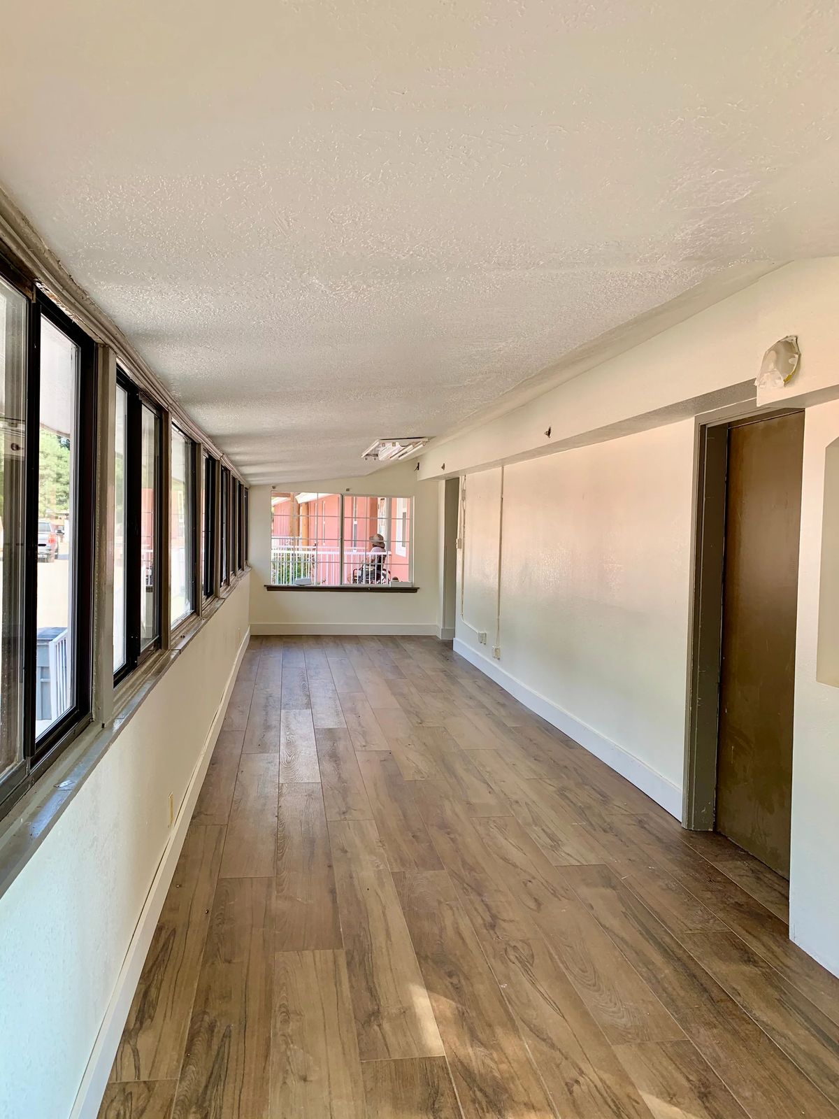 A well-lit corridor with wooden flooring and large windows.