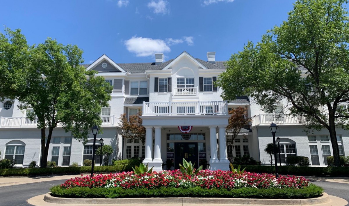 A charming hotel building with well-maintained landscaping, featuring vibrant flowers and lush trees under a clear sky.