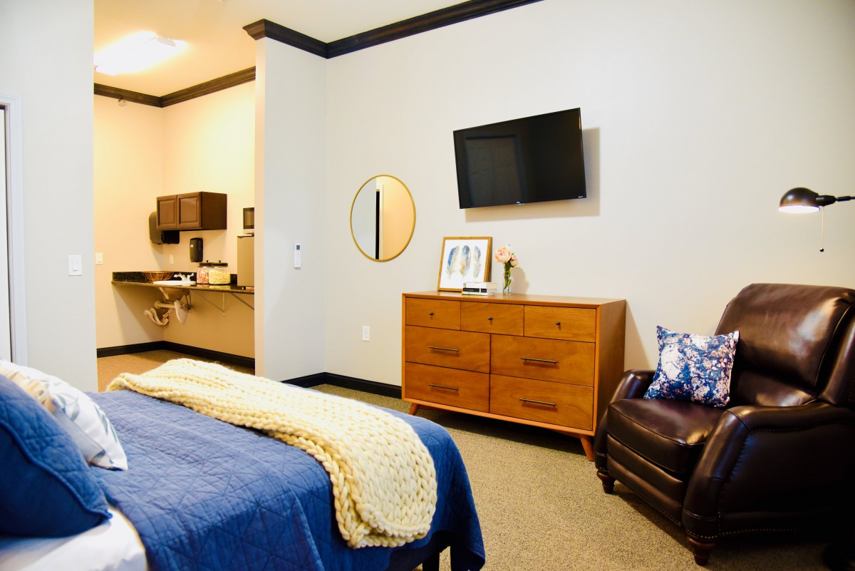 A modern bedroom interior featuring a bed with blue bedding, a dresser with decorative items, and a wall-mounted television.