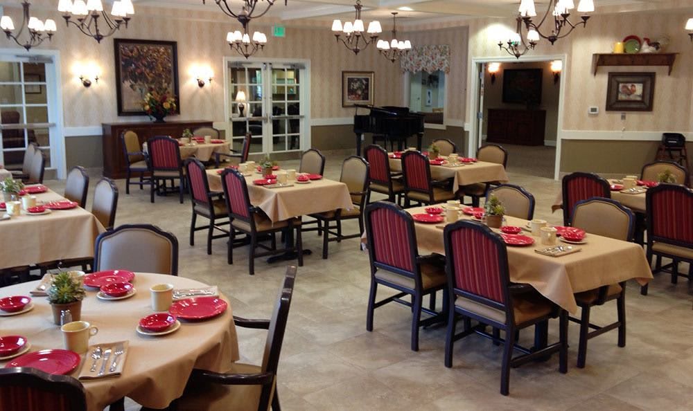 An elegantly decorated dining room with neatly arranged tables and chairs, featuring chandeliers and a grand piano in the background.