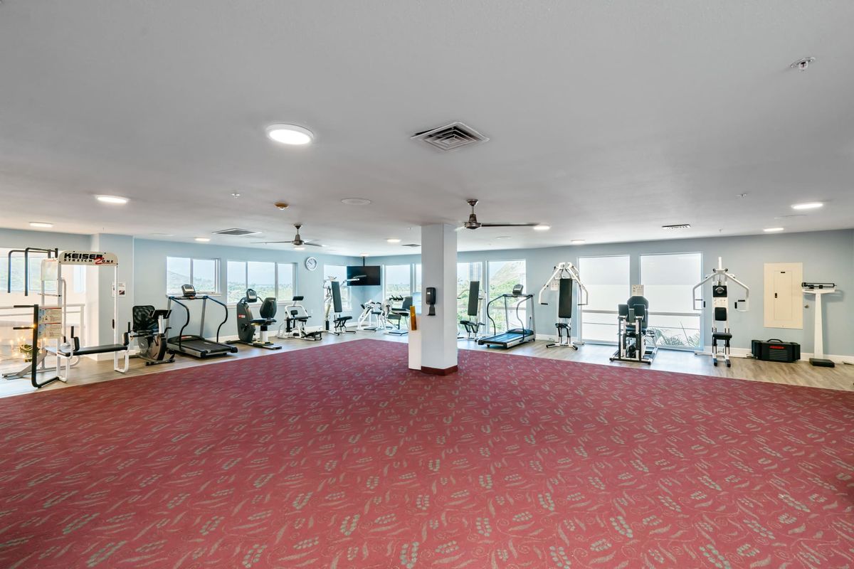 A spacious gym with various exercise equipment including treadmills and stationary bikes, surrounded by large mirrors.