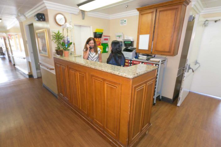 Two people conversing at a reception desk in an office setting.