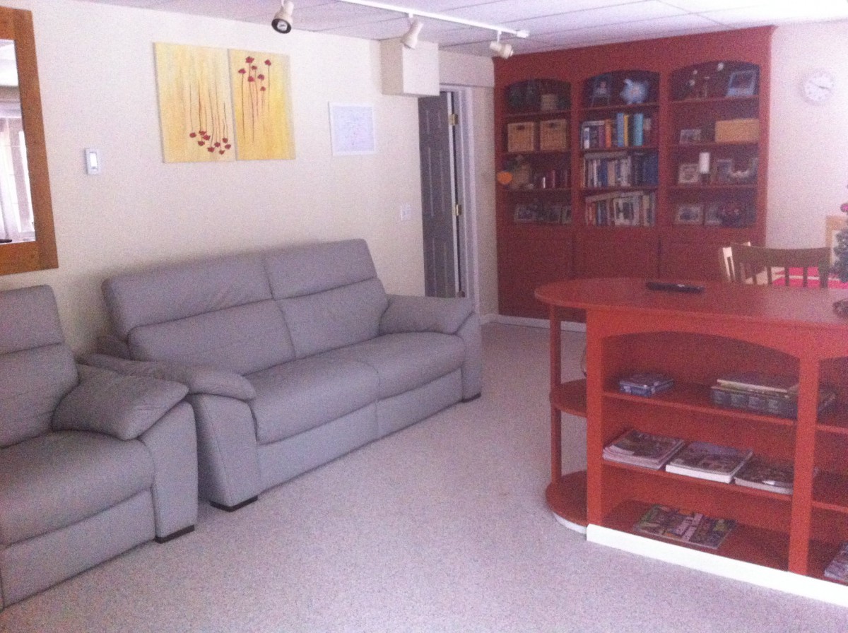 A cozy living room featuring a grey sofa, carpeted floor, and a wooden bookshelf.