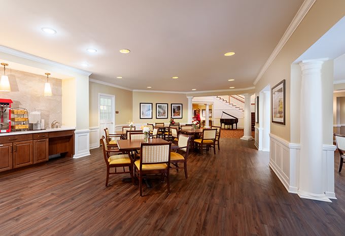 A well-lit dining room with wooden flooring, featuring multiple tables and chairs arranged neatly.