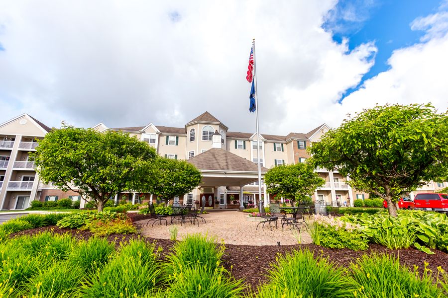 A beautiful building with a well-maintained garden and flags flying in front, set against a partly cloudy sky.