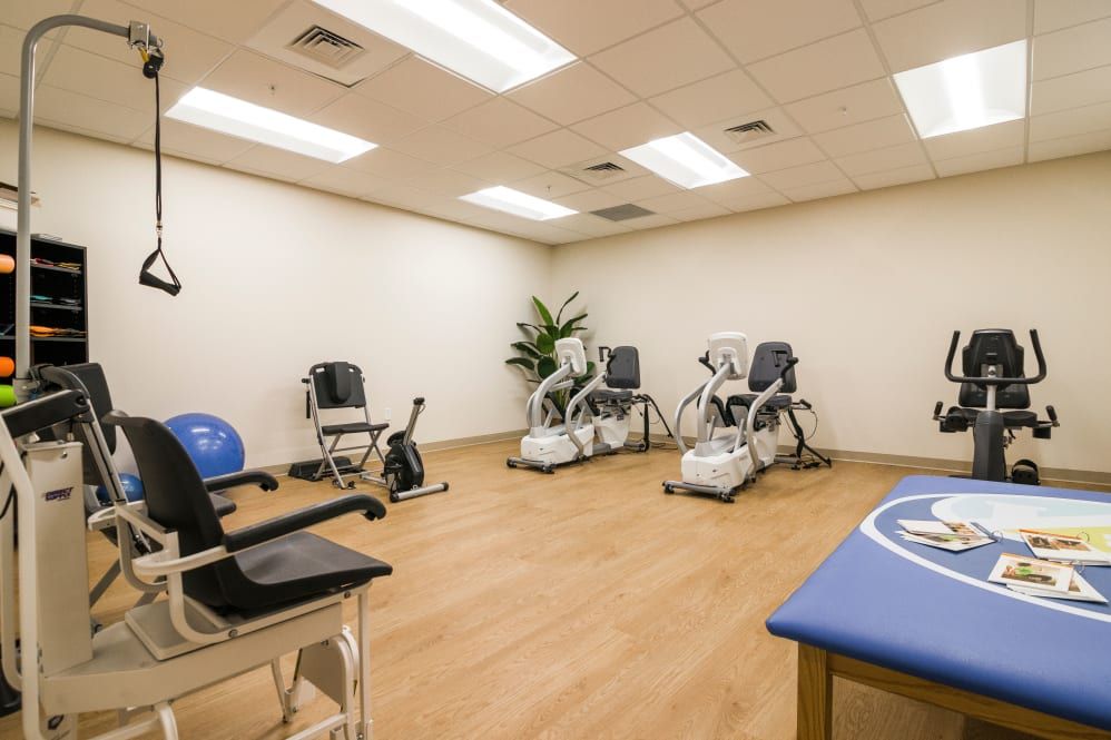 A rehabilitation room equipped with various exercise machines and chairs.