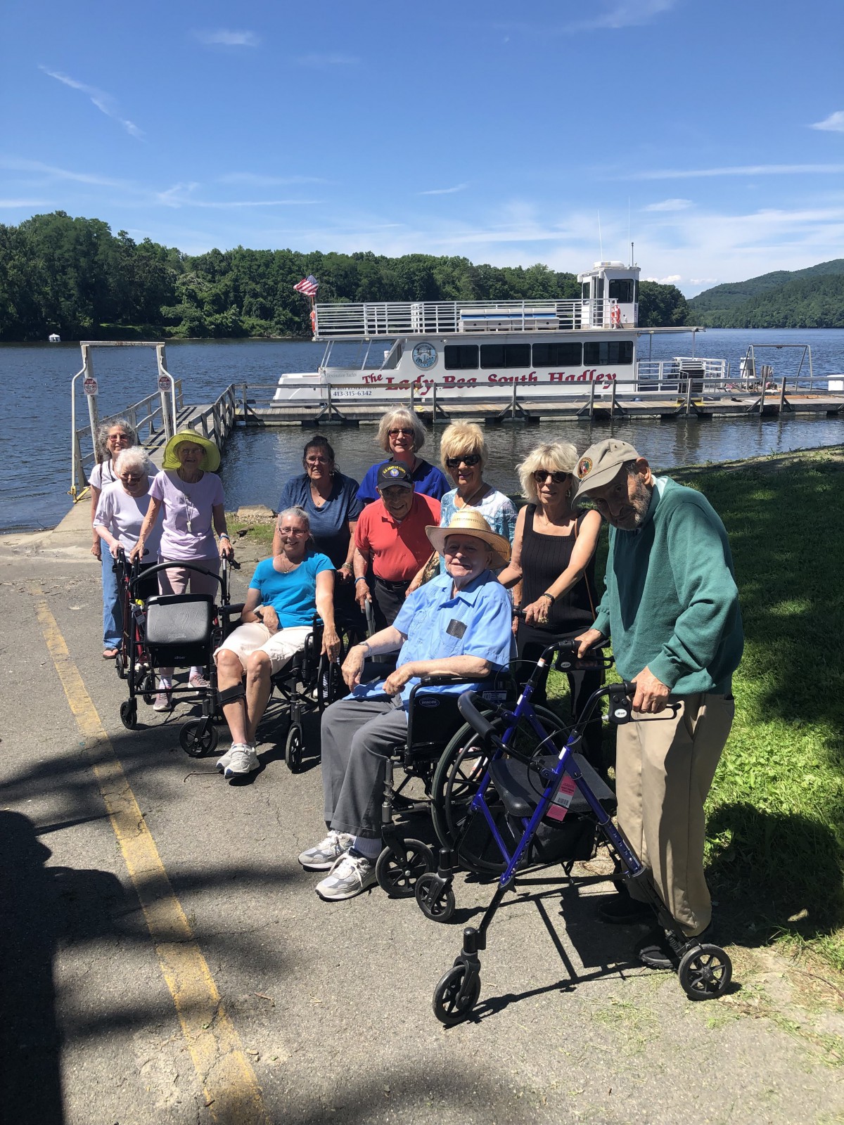 A group of seniors enjoying a day by the lake, some using wheelchairs.