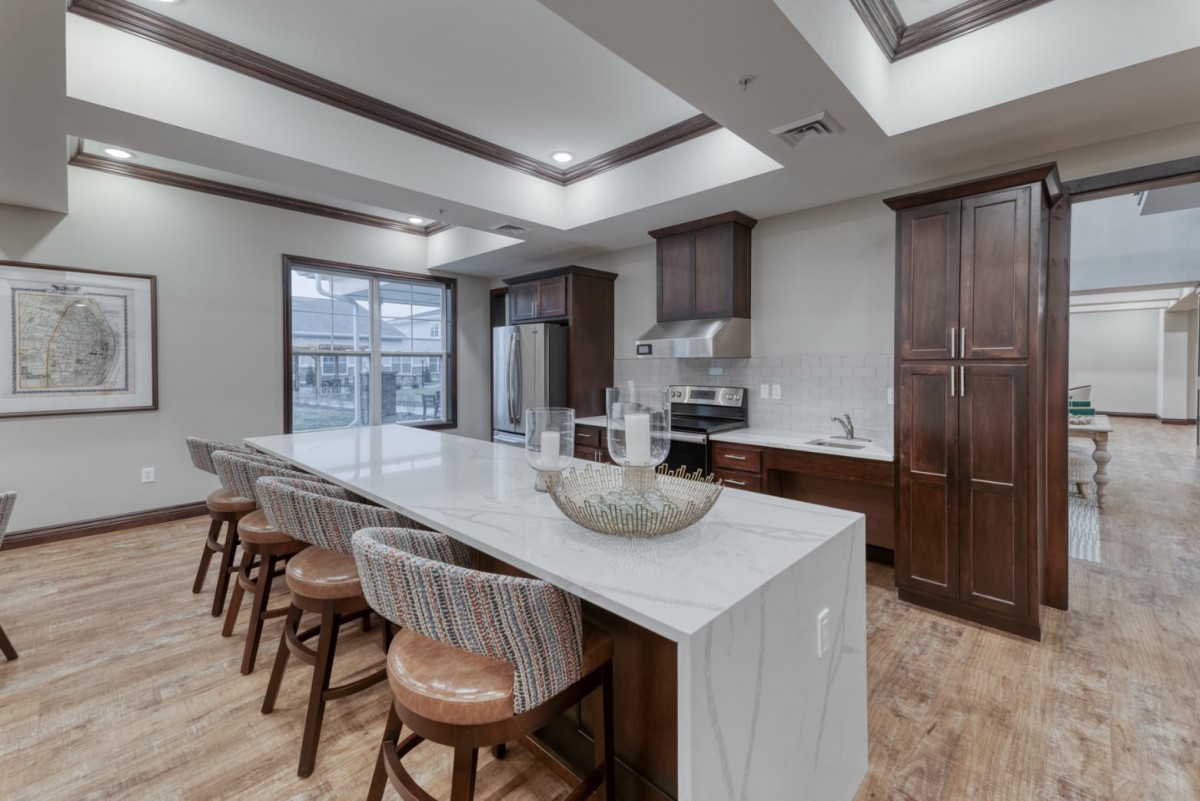 A modern kitchen featuring a large island counter with bar stools, wood cabinets, and stainless steel appliances.