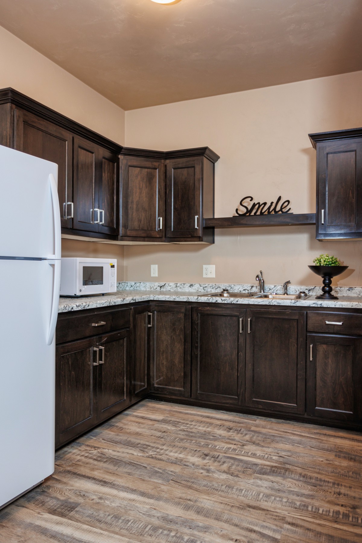 A modern kitchen with dark wood cabinets, a white refrigerator, and a microwave.