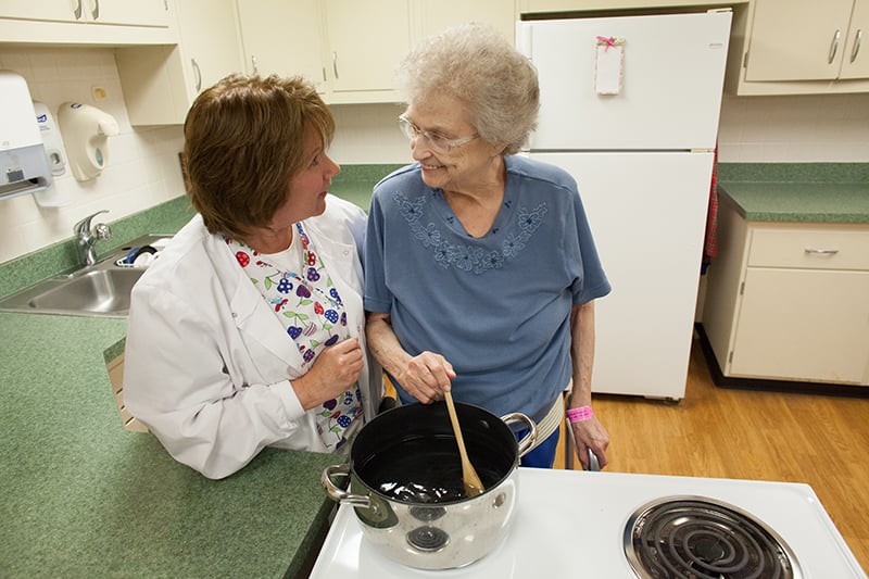 An elderly woman and a caregiver are engaged in cooking together, sharing a moment in the kitchen.