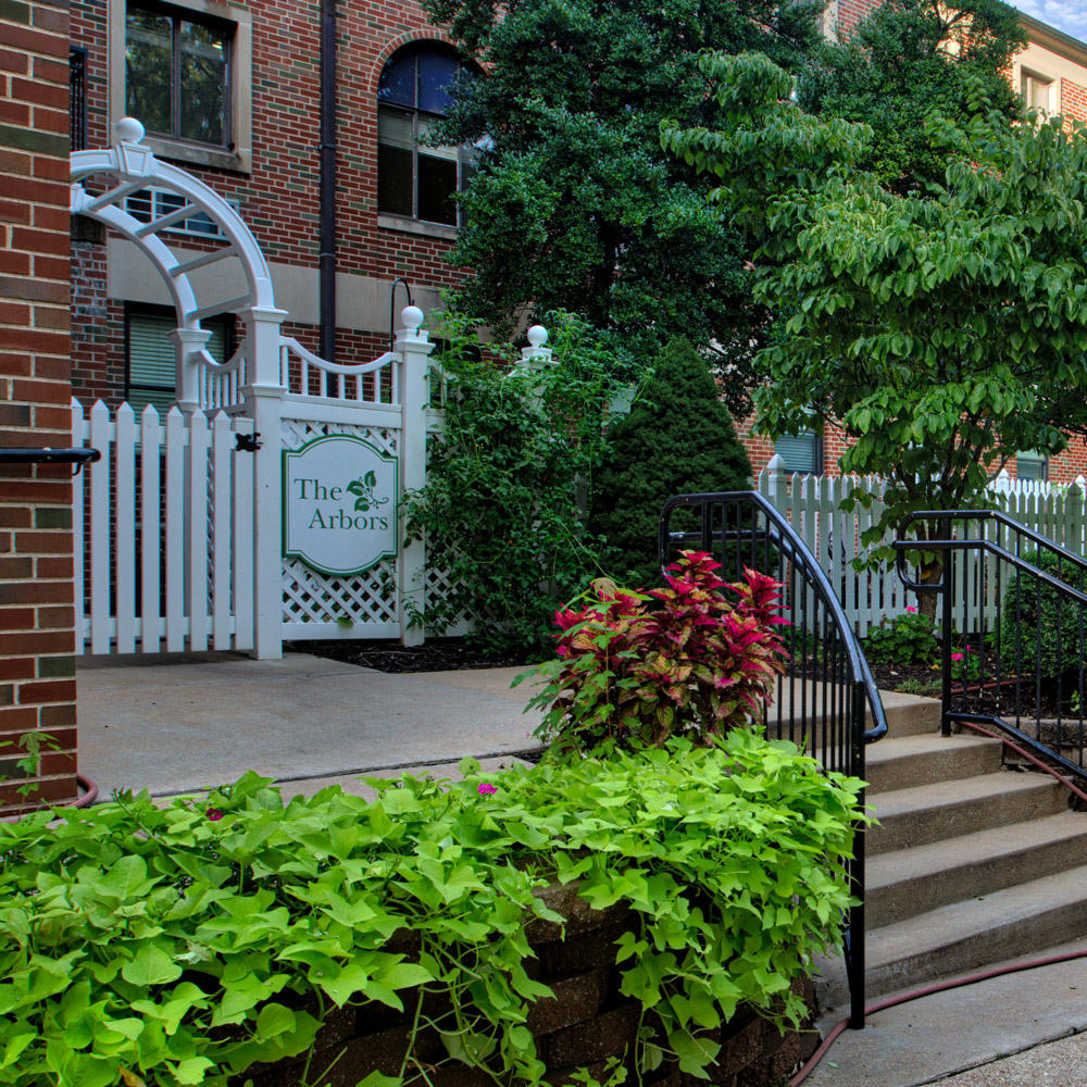 A charming entrance gate surrounded by lush greenery and a brick building.