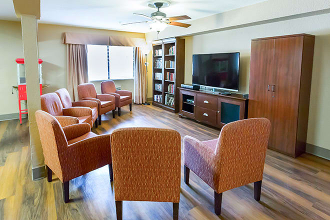 A cozy living room with multiple chairs arranged around a television set, complete with a ceiling fan and bookshelf.