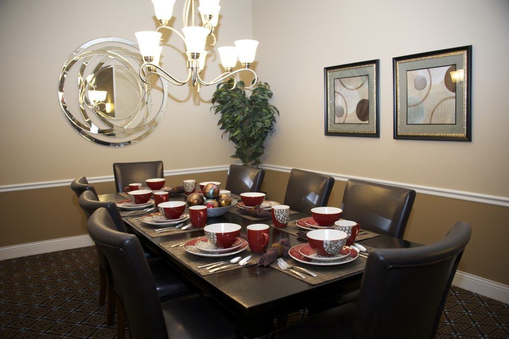 A well-decorated dining room with a formal table setting, featuring red dishware and an elegant chandelier.