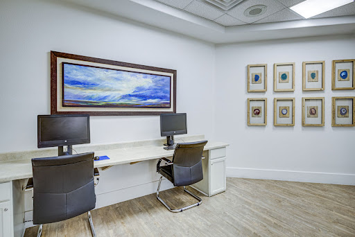 A modern office space featuring a desk with computers, stylish chairs, and framed artwork on the walls.