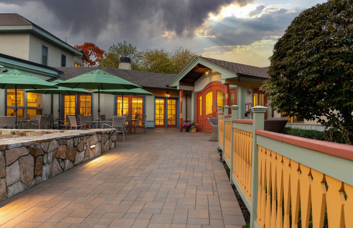 A charming patio at a restaurant during evening hours, illuminated by warm lights under a cloudy sky.