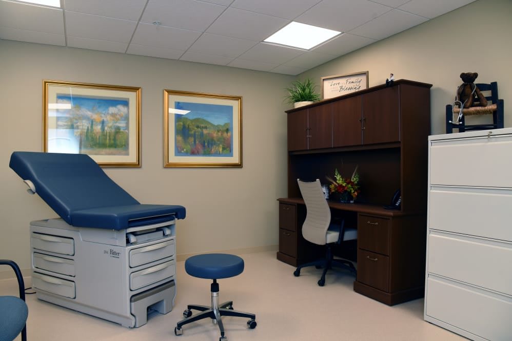 A well-organized doctor's office with an examination table, a stool, and a desk.