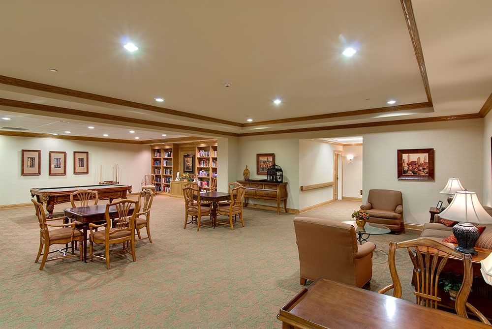 A cozy library room with tables, chairs, and bookshelves.