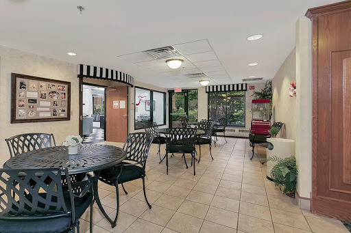 A cozy dining area with tables and chairs, featuring large windows and decorative plants.