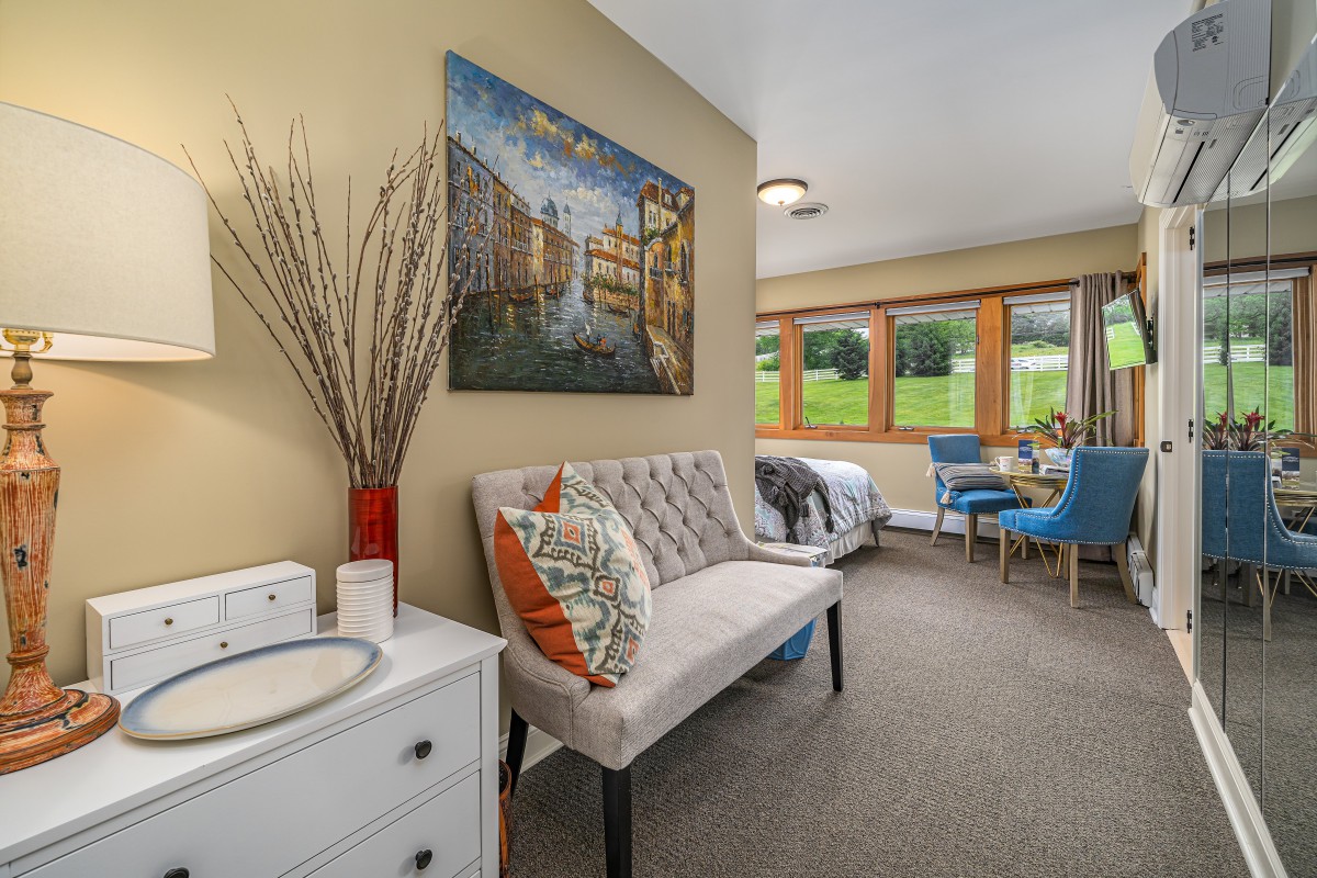 A cozy living space featuring a stylish sofa with decorative pillows, vibrant artwork on the wall, and large windows inviting natural light.