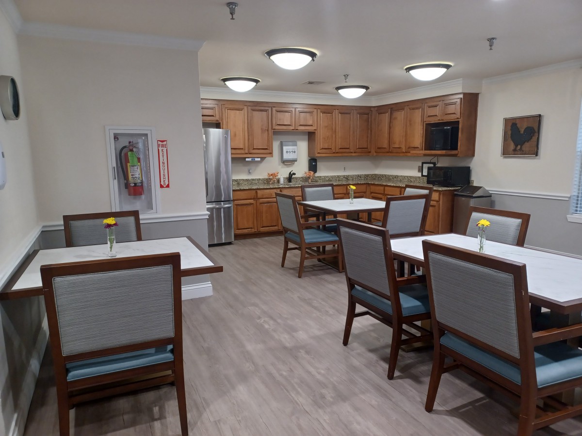 A spacious kitchen and dining area with wooden cabinets, modern lighting, and neatly arranged tables and chairs.