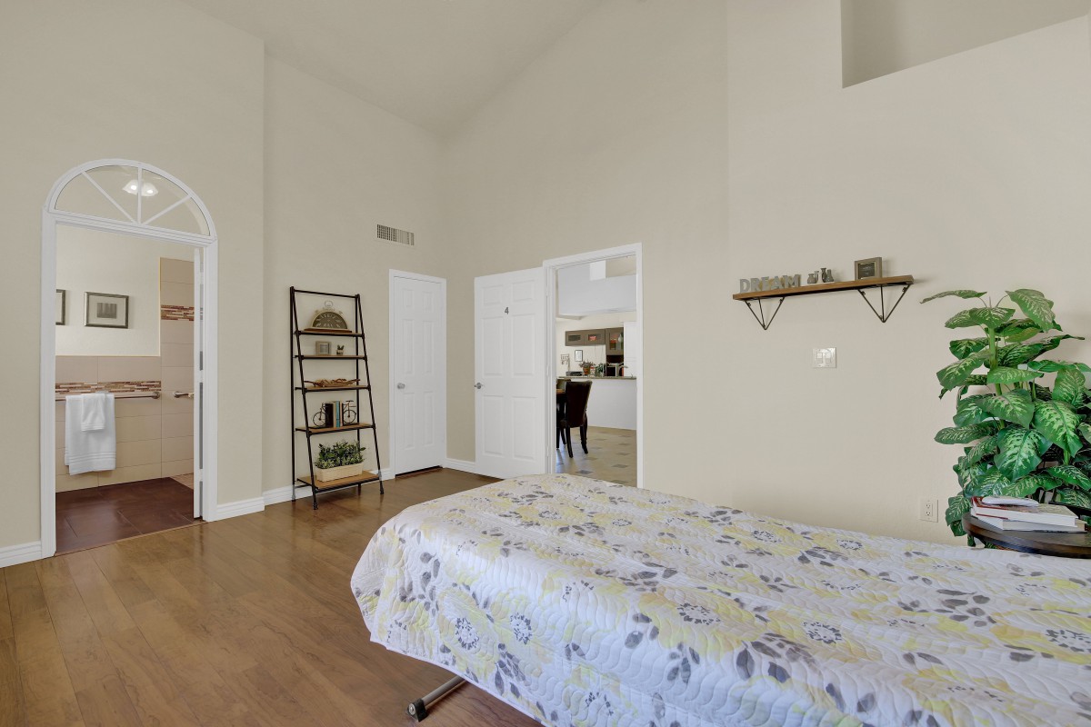 A cozy bedroom with a neatly made bed, wooden floors, and decorative shelves.