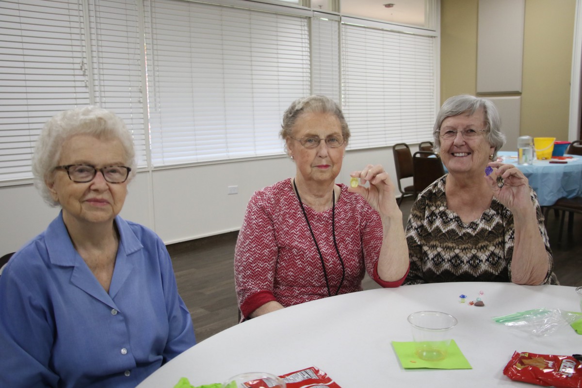 Three elderly women sitting at a table with playing cards.