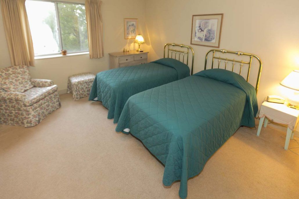 A cozy bedroom with twin beds featuring green bedspreads and a nightstand with a lamp.