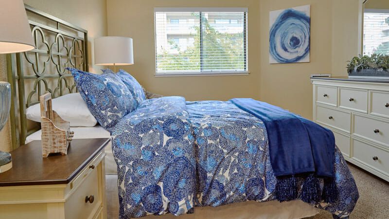 A cozy bedroom with blue-patterned bedding, a window view, and matching decor.