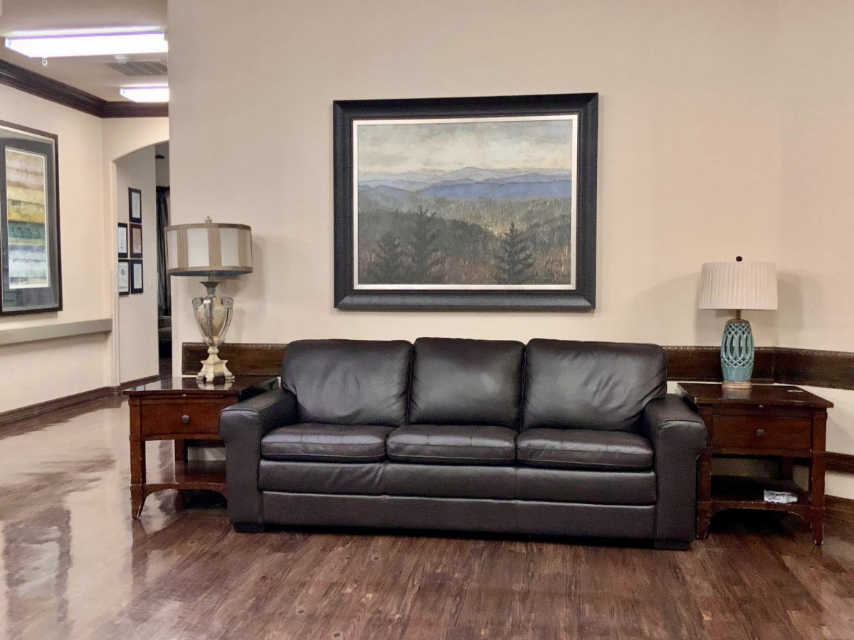 A cozy living room setting featuring a dark sofa, side tables with lamps, and a landscape painting on the wall.