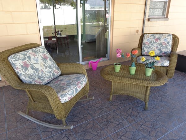 A cozy outdoor patio setup with wicker chairs and a table decorated with colorful potted plants.