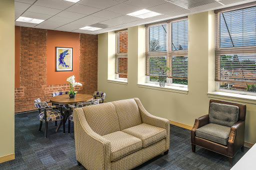 A cozy office lounge area featuring soft seating, a dining table, and large windows allowing natural light.