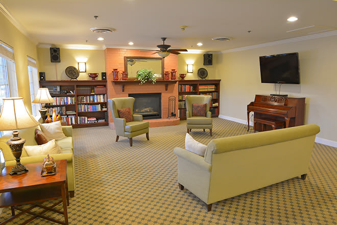 A cozy living room with a central fireplace, surrounded by bookshelves and comfortable seating, featuring a piano in the corner.