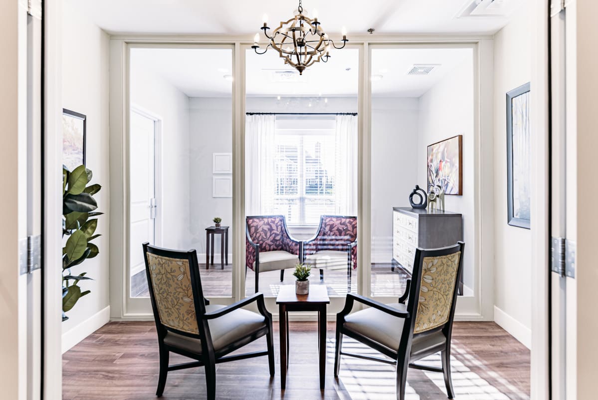 A modern living room with two chairs facing each other, separated by a small table, under a stylish chandelier.