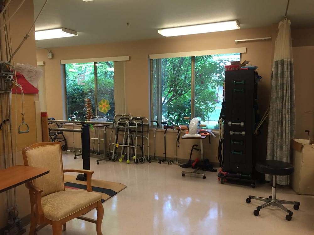 A quiet healthcare facility room with walkers and chairs by large windows.