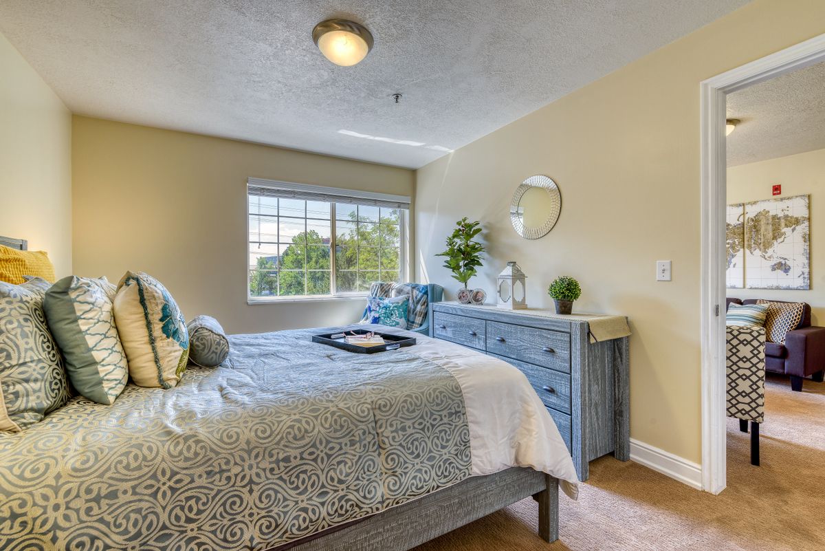 A cozy bedroom with a neatly made bed, blue dresser, and decorative plants.