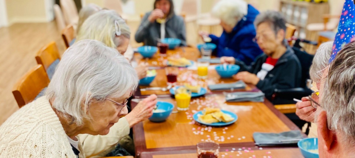 A group of elderly individuals enjoying a meal together at a communal dining table.