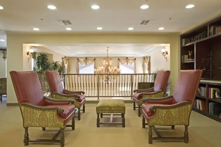 Elegant seating area with armchairs overlooking a chandelier-lit space.