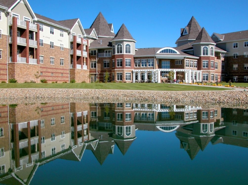 A modern residential building with a castle-like design reflected in a calm lake.