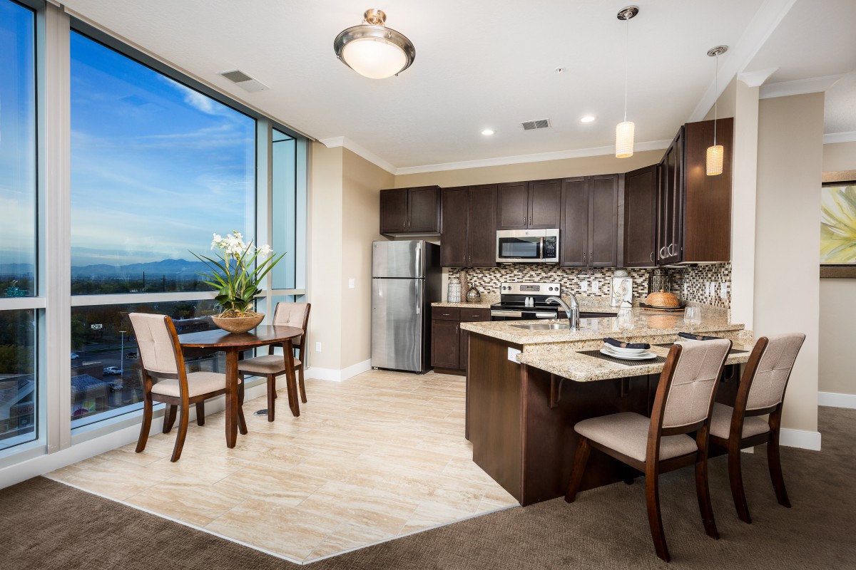 A modern apartment kitchen and dining area with elegant furnishings and a large window providing natural light.