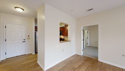 A modern interior featuring an open layout with a view into the kitchen, showcasing hardwood floors and neutral colors.