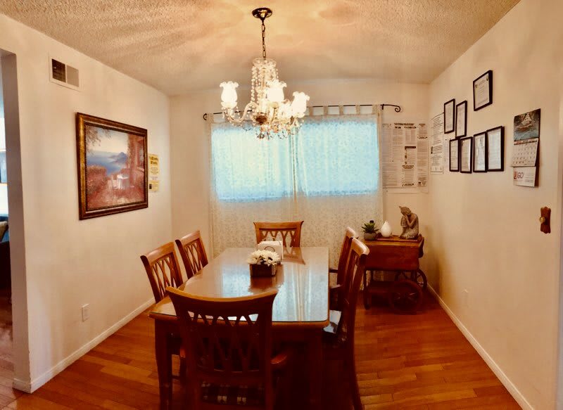 A cozy dining room featuring a wooden table set, elegant chandelier, and tasteful artwork on the walls.