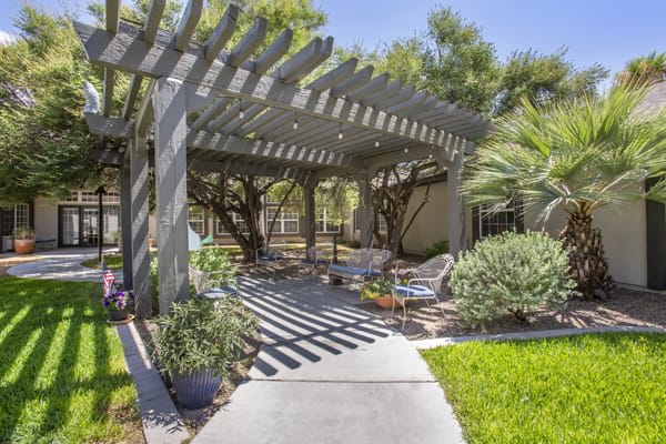 A serene outdoor patio area with a pergola, surrounded by lush greenery and comfortable seating.