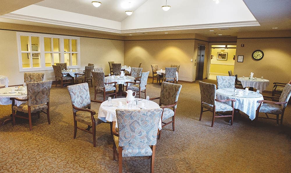 An elegant dining room with round tables and upholstered chairs, set for service.