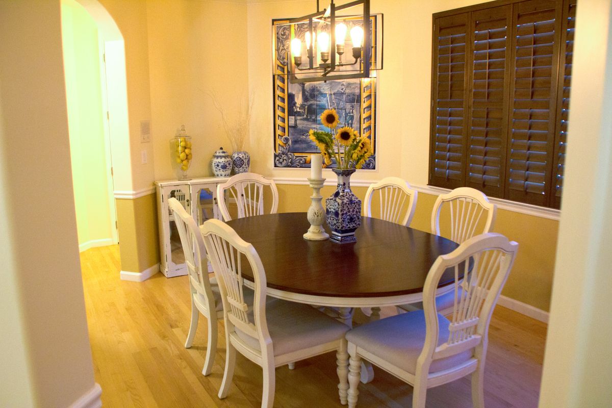A cozy dining room with a round table, elegant white chairs, and a vase of sunflowers as the centerpiece.