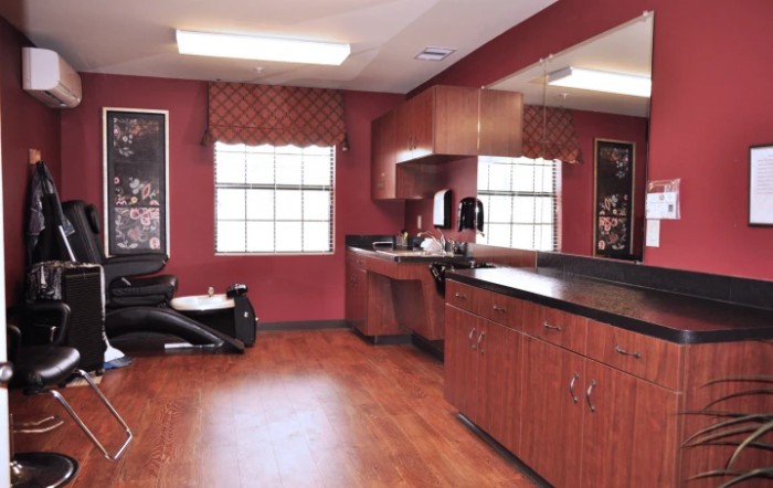 An empty barber shop with red walls, mirrors, and cabinets.