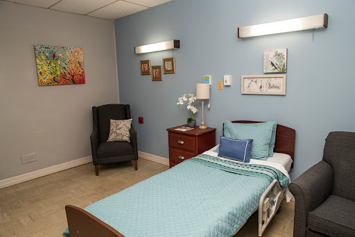 A cozy hospital room featuring a single bed, comfortable chair, and decorative wall art.