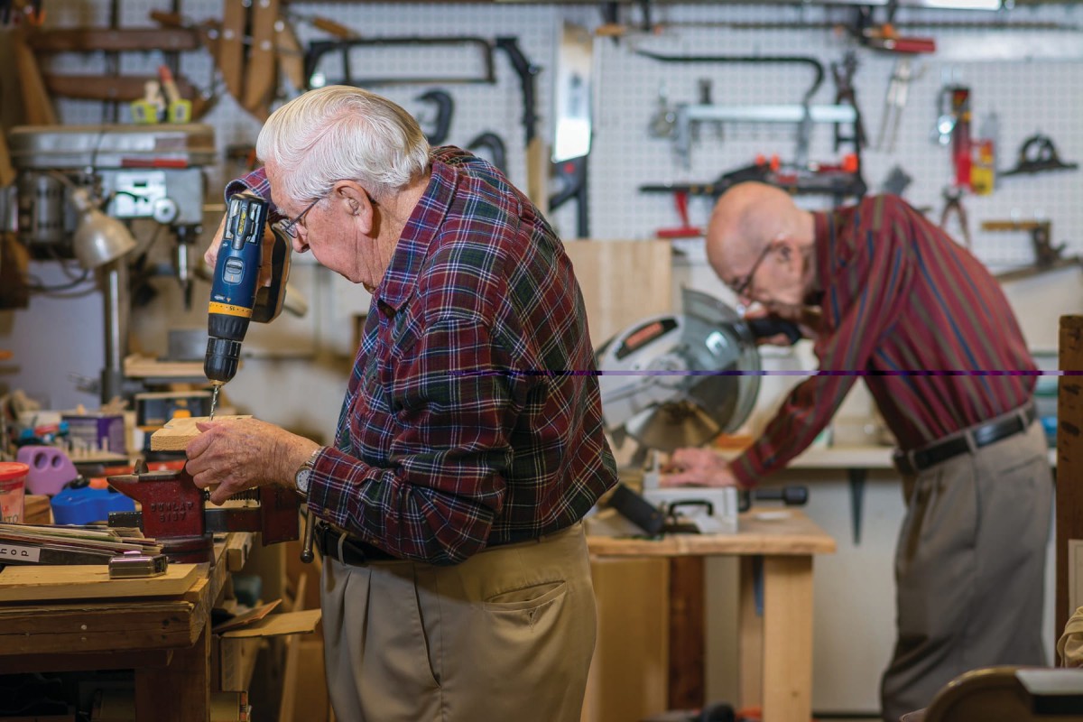 Two elderly men working on projects in a woodworking workshop.